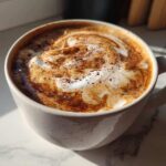 Close-up of a creamy Banana Bread Latte topped with foamed milk swirl and cinnamon spice.