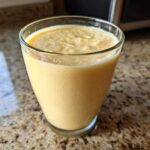 A close-up of a thick, creamy Banana Chamomile Tea Smoothie served in a clear glass on a granite countertop.