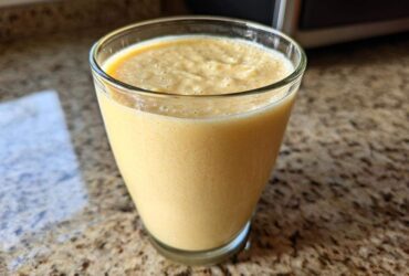 A close-up of a thick, creamy Banana Chamomile Tea Smoothie served in a clear glass on a granite countertop.
