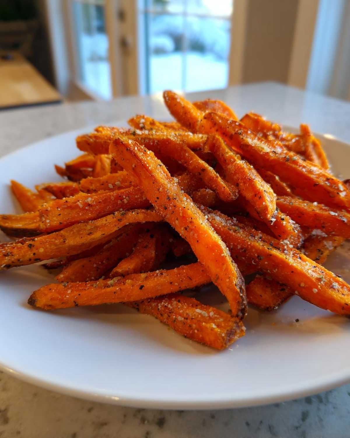 A close-up of a pile of Best Ever Crispy Oven Baked Sweet Potato Fries seasoned with salt and pepper on a white plate.