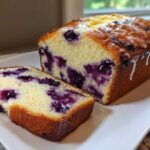 A sliced Blueberry Cream Cheese Bread Loaf with a sweet glaze drizzled over the top, showing rich interior blueberries.