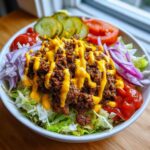 A close-up of a fresh Burger Bowls 30 Minute Dinner Idea featuring seasoned ground beef, cheese sauce, lettuce, onions, pickles, and ketchup.