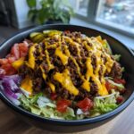 A close-up of a hearty Burger Bowls 30 Minute Dinner Idea featuring seasoned ground beef, melted cheese sauce, lettuce, tomatoes, and red onion.