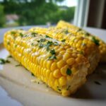 Close-up of three ears of bright yellow Buttered Corn glistening with melted butter and topped with fresh parsley.