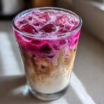 Close-up of a layered Cherry Vanilla Iced Latte featuring bright pink cherry syrup mixing with creamy milk and coffee over ice.