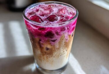 Close-up of a layered Cherry Vanilla Iced Latte featuring bright pink cherry syrup mixing with creamy milk and coffee over ice.