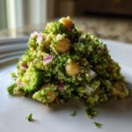 A mound of vibrant Chopped Broccoli and Chickpea Salad featuring finely chopped broccoli, chickpeas, and red onion on a white plate.