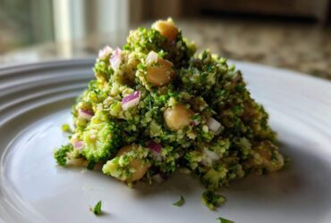 A mound of vibrant Chopped Broccoli and Chickpea Salad featuring finely chopped broccoli, chickpeas, and red onion on a white plate.