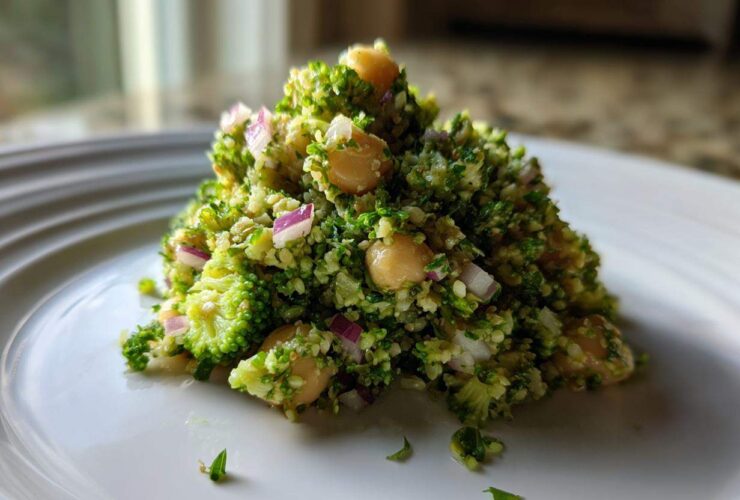 A mound of vibrant Chopped Broccoli and Chickpea Salad featuring finely chopped broccoli, chickpeas, and red onion on a white plate.
