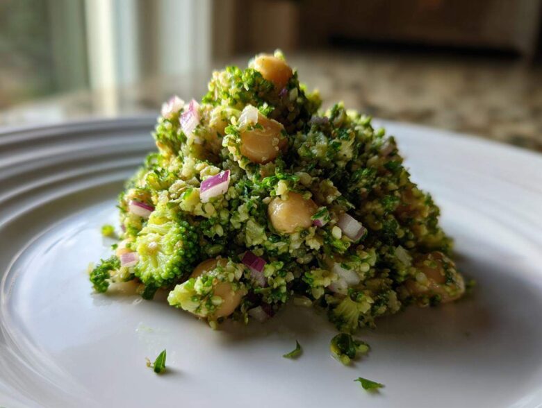 A mound of vibrant Chopped Broccoli and Chickpea Salad featuring finely chopped broccoli, chickpeas, and red onion on a white plate.