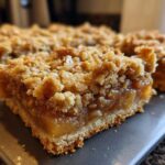 A close-up view of a thick, fudgy Apple Bars slice showing the gooey apple filling and crumbly oat topping.