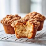 A close-up of a Coffee Cake Muffin with a bite taken out, showing the moist interior and thick cinnamon streusel topping.
