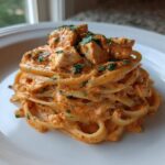 A close-up of creamy Cajun chicken pasta served on a white plate, garnished with fresh parsley.