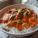 A white bowl filled with fluffy white rice topped generously with rich, orange Creamy Garlic Tikka Masala Sauce and fresh cilantro.