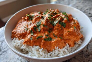 A white bowl filled with fluffy white rice topped generously with rich, orange Creamy Garlic Tikka Masala Sauce and fresh cilantro.