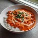A white bowl filled with fluffy white rice topped generously with vibrant orange Creamy Garlic Tikka Masala Sauce, swirled with cream and fresh cilantro.