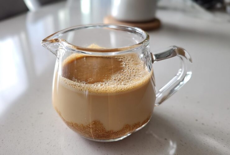 A small glass pitcher containing homemade Creme Brulee Coffee Creamer with undissolved brown sugar visible at the bottom.
