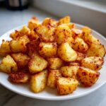 A close-up of perfectly seasoned and crispy Air Fryer Potatoes piled high on a white plate.