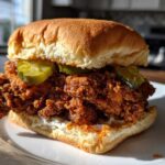 A close-up of a thick, juicy Crispy Chicken Sandwich featuring heavily breaded chicken, pickles, and sauce on a brioche bun.