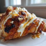 A close-up of Crispy Hot Honey Feta Chicken, glazed and topped with white feta cheese crumbles and sauce.