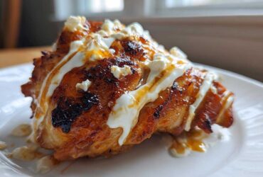 A close-up of Crispy Hot Honey Feta Chicken, glazed and topped with white feta cheese crumbles and sauce.
