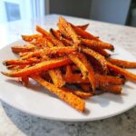 A close-up of a pile of Best Ever Crispy Oven Baked Sweet Potato Fries seasoned with salt and spices on a white plate.