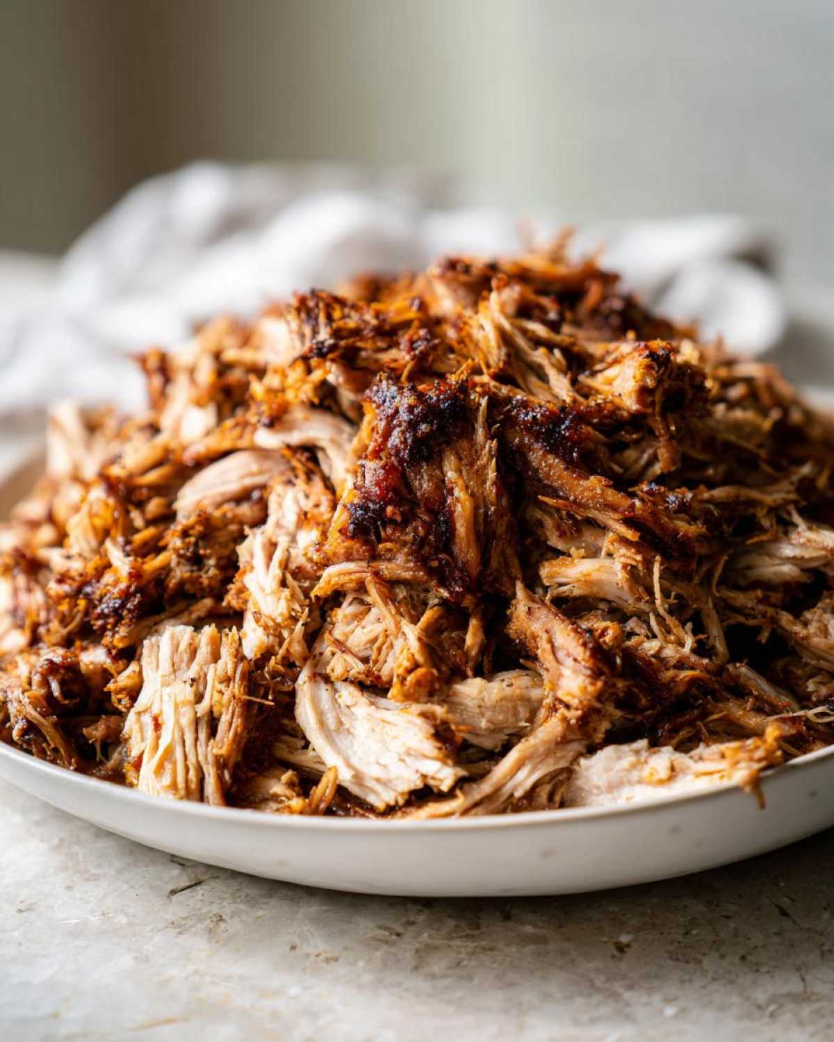 A close-up shot of a large mound of shredded, crispy Slow Cooker Carnitas piled high on a white serving dish.