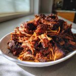 A mound of deeply browned and shredded Crispy Slow Cooker Carnitas piled high on a white serving dish.