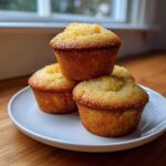 A stack of four golden brown Crushed Pineapple Muffins with sugary tops resting on a white plate.