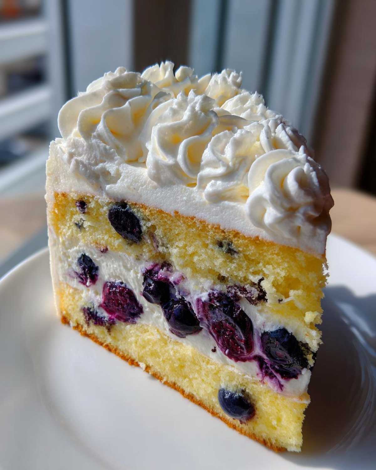 A perfect slice of Fluffy Lemon Blueberry Naked Cake Homemade with Whipped Cream Frosting on a white plate.