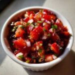 A close-up of vibrant, chunky Strawberry Salsa featuring diced strawberries, red onion, and cilantro in a small white ramekin.