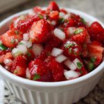Close-up of vibrant Strawberry Salsa featuring diced strawberries, white onion, and cilantro in a small white bowl.