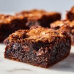 Close-up of a rich, fudgy brownie square with a shiny, crackly top, showing melted chocolate chips. Ideal for making Brookies.