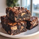 Close-up of fudgy Kit Kat Brownies stacked, showing chocolate chips and chunks of Kit Kat candy baked inside.