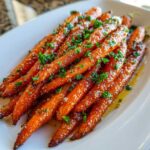 Close-up of shiny Glazed Honey Garlic Butter Roasted Carrots topped with fresh parsley on a white serving dish.