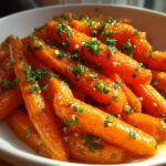 Close-up of vibrant orange Glazed Honey Garlic Butter Roasted Carrots topped with fresh parsley in a white serving bowl.