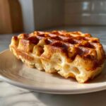 Close-up of a perfectly cooked, golden brown Belgian Waffles showing its airy interior texture on a white plate.