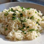 A close-up of fluffy Greek Lemon Rice topped with fresh chopped parsley and lemon zest.