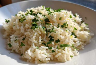 A close-up of fluffy Greek Lemon Rice topped with fresh chopped parsley and lemon zest.