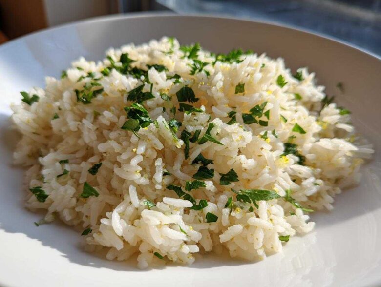 A close-up of fluffy Greek Lemon Rice topped with fresh chopped parsley and lemon zest.