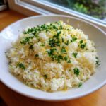 A white bowl filled with fluffy Greek Lemon Rice, topped generously with chopped parsley and bright yellow lemon zest.