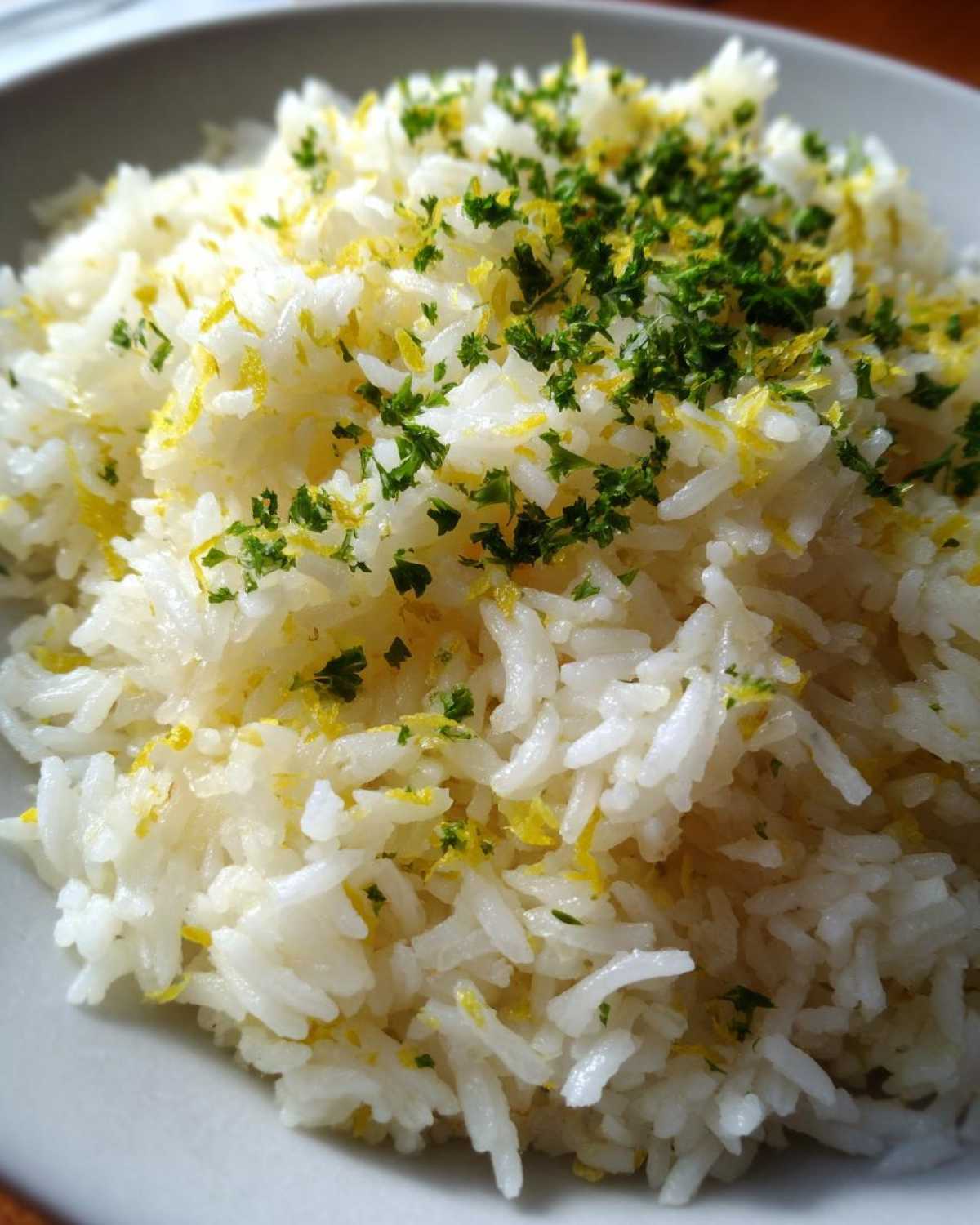 Close-up of fluffy white Greek Lemon Rice topped with bright yellow lemon zest and chopped green parsley.
