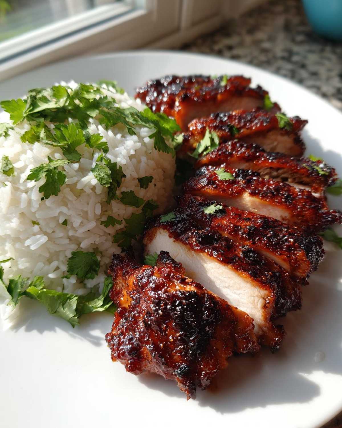 Slices of glazed Hawaiian Chicken served next to a mound of white coconut rice topped with fresh cilantro.