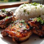 Four pieces of glazed Hawaiian Chicken served next to a mound of fluffy Coconut Rice, garnished with fresh herbs.