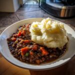 A bowl featuring rich Hearty Lentil Stew with Creamy Mashed Potatoes, seasoned with pepper.
