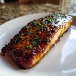 A close-up of a perfectly cooked Honey Garlic Glazed Salmon fillet, glistening with sauce and topped with fresh parsley.