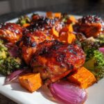 Close-up of glazed Honey Harissa Chicken thighs served with roasted broccoli, sweet potatoes, and red onion.