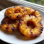 Four caramelized rings of Honey Lime Roasted Pineapple glistening on a white plate.