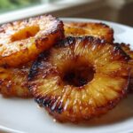 Close-up of caramelized Honey Lime Roasted Pineapple rings stacked on a white plate, showing glossy, browned edges.