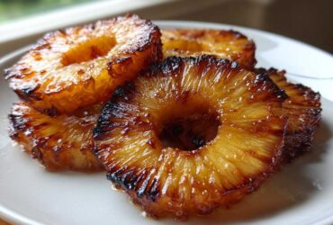 Close-up of caramelized Honey Lime Roasted Pineapple rings stacked on a white plate, showing glossy, browned edges.